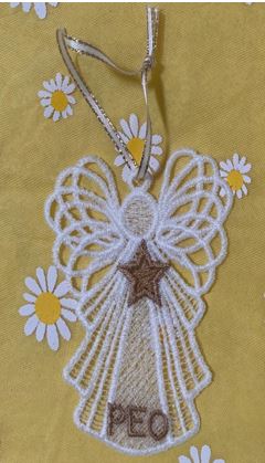 Handcrafted macrame angel ornament with a star, hanging against a yellow floral background.